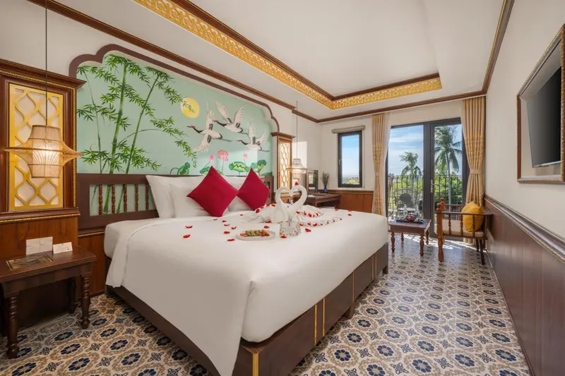 Chambre lumineuse avec un grand lit décoré de pétales de fleurs et une vue sur la végétation.