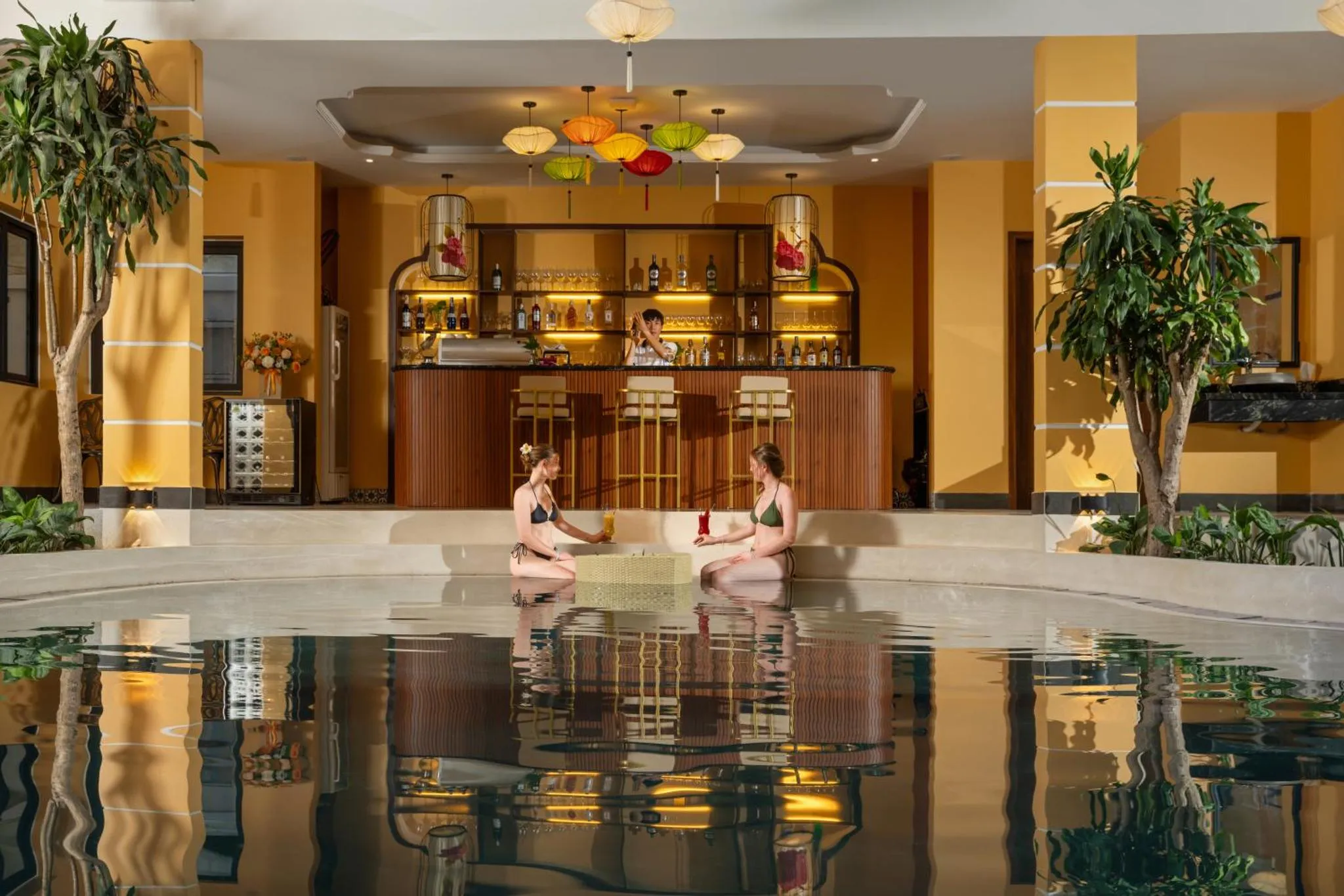 Deux femmes sont assises au bord d'une piscine avec des boissons, devant un bar.