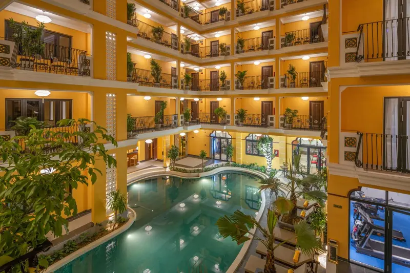 Vue d'une cour intérieure d'hôtel avec une piscine et des balcons fleuris.