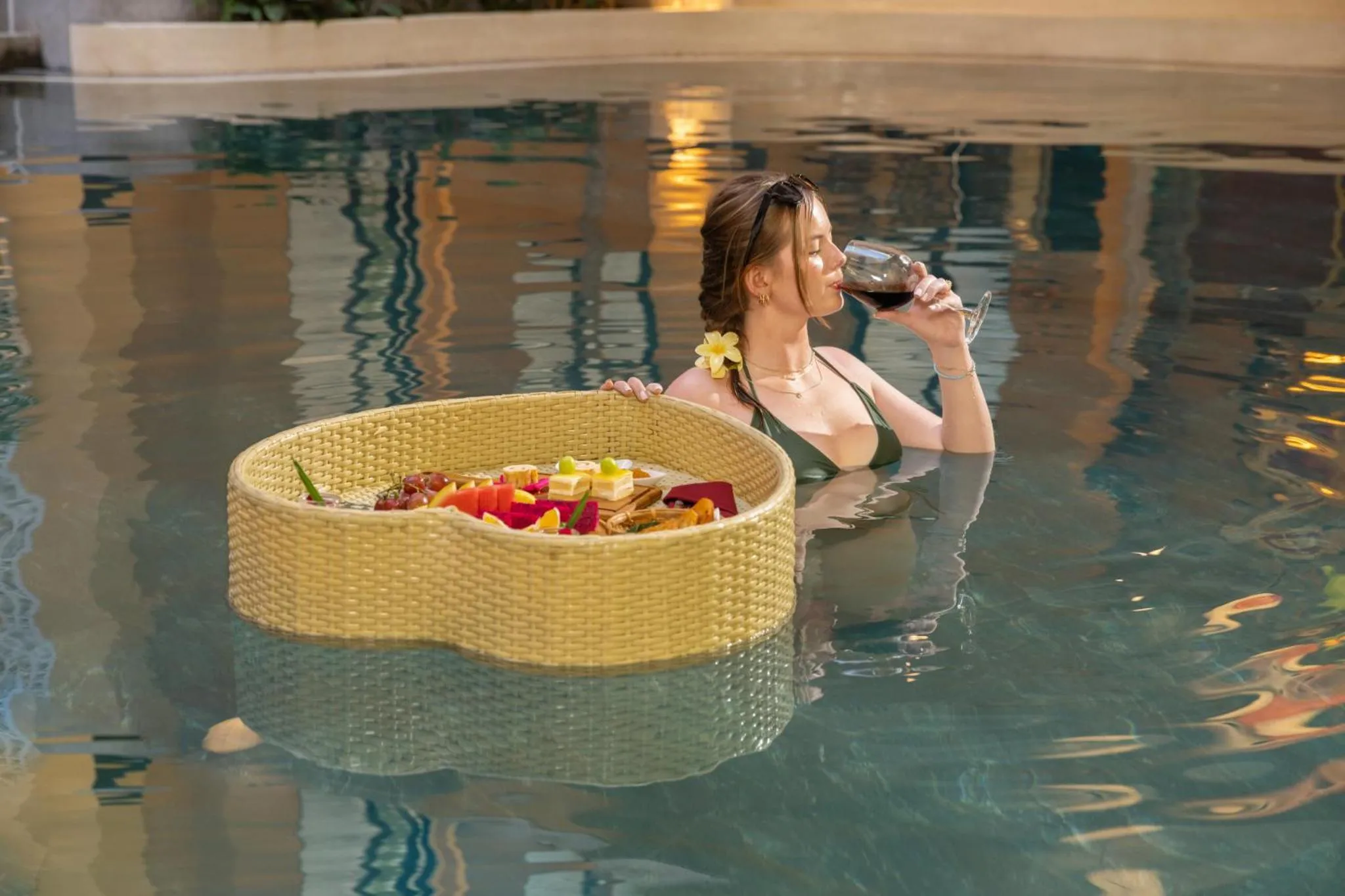 Une femme se détend dans une piscine avec un plateau de nourriture et une boisson.