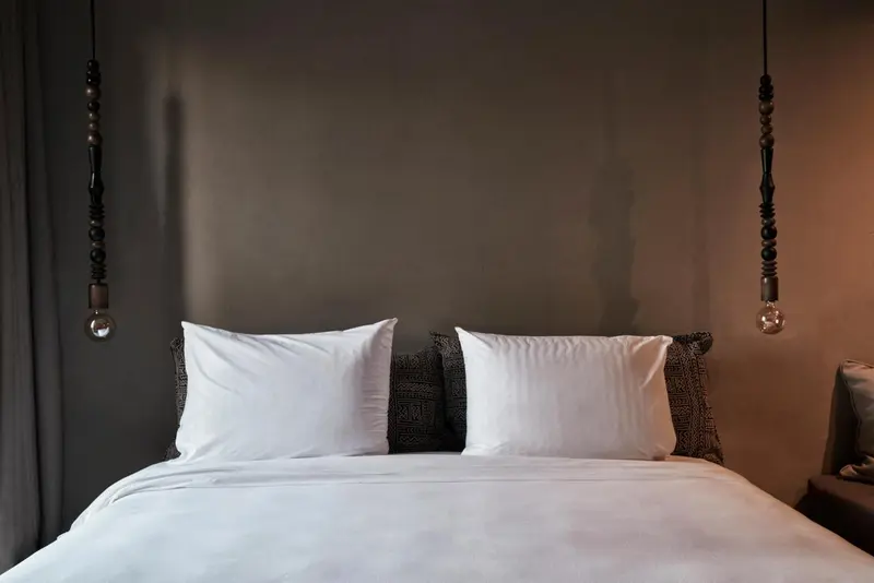 Un lit double avec des oreillers blancs et une literie soignée dans une chambre aux murs gris.