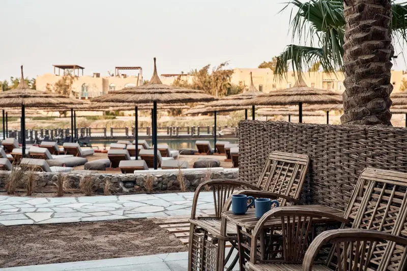 Terrasse avec mobilier en rotin et parasols en chaume face à une piscine.