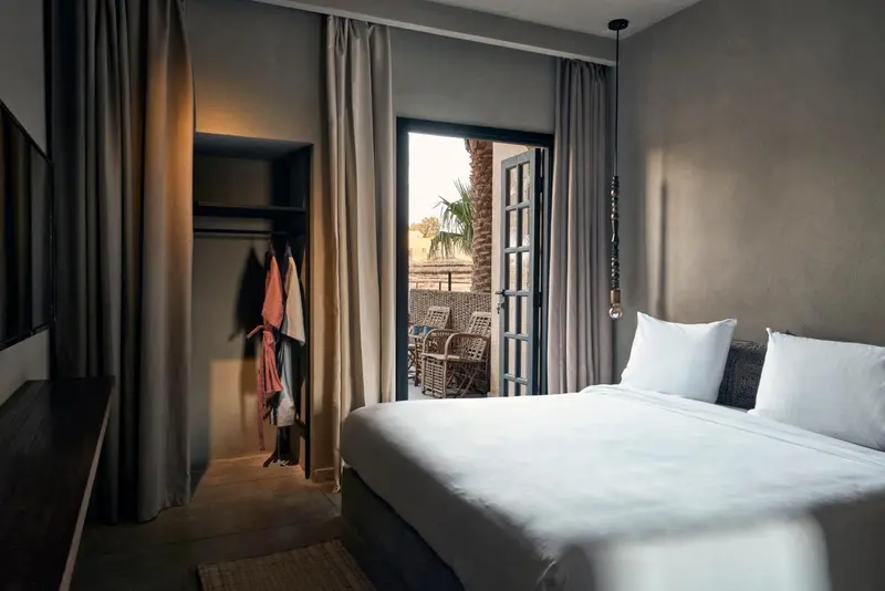 Une chambre lumineuse avec un lit blanc et un accès à un balcon.