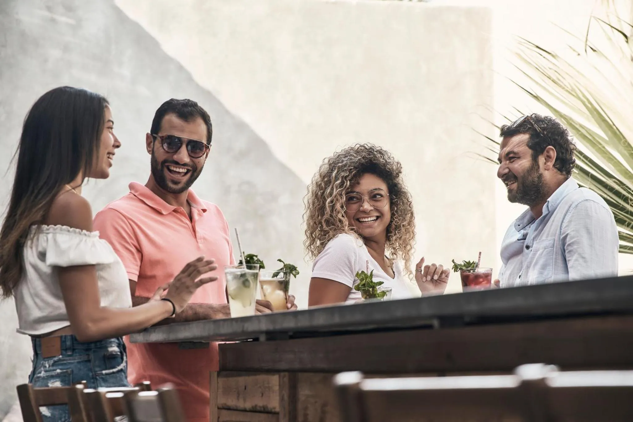 Quatre personnes sourient et discutent autour d'une table en extérieur avec des boissons.