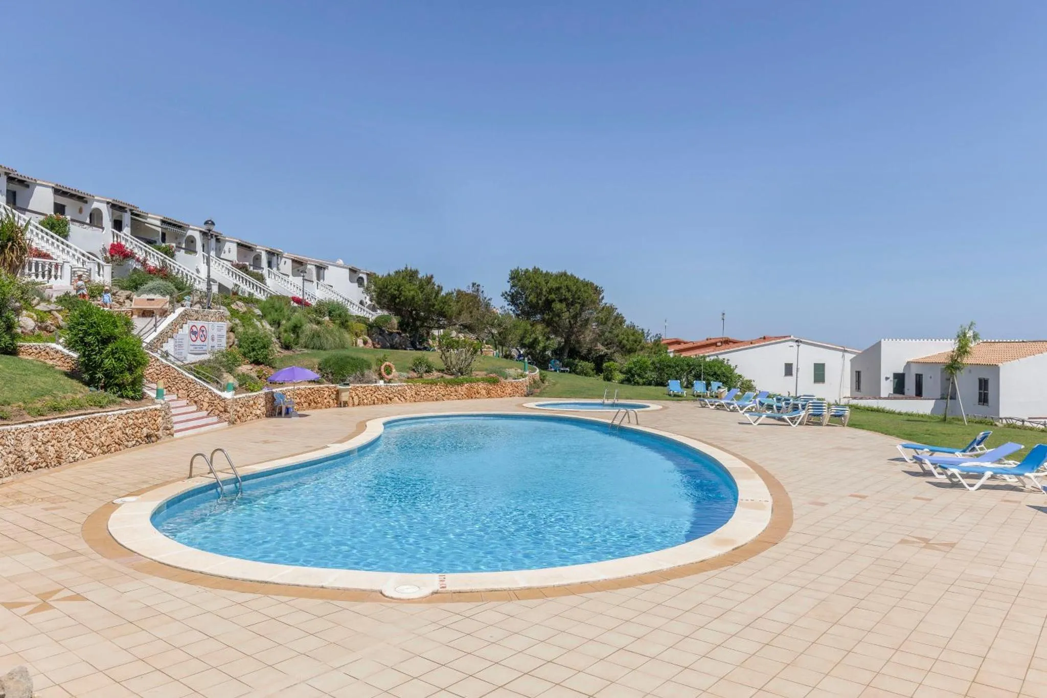 Une piscine rectangulaire bordée de transats et de végétation.