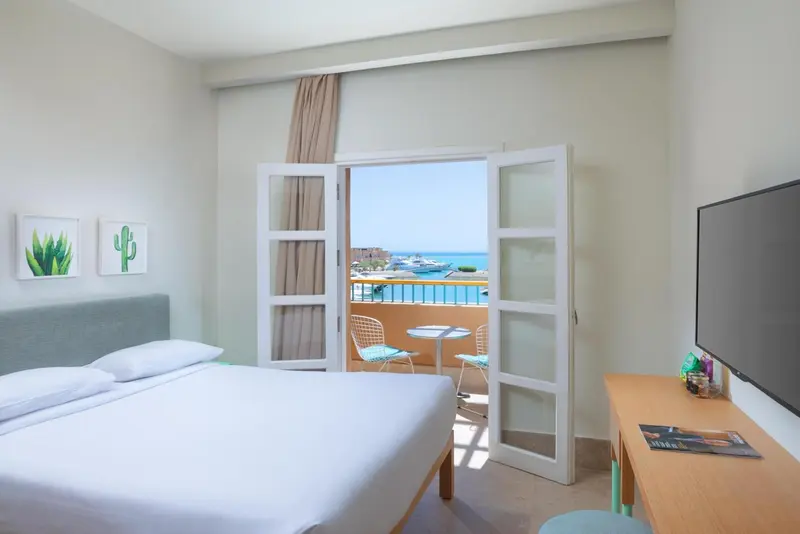Une chambre lumineuse avec un lit blanc et un balcon donnant sur la mer.