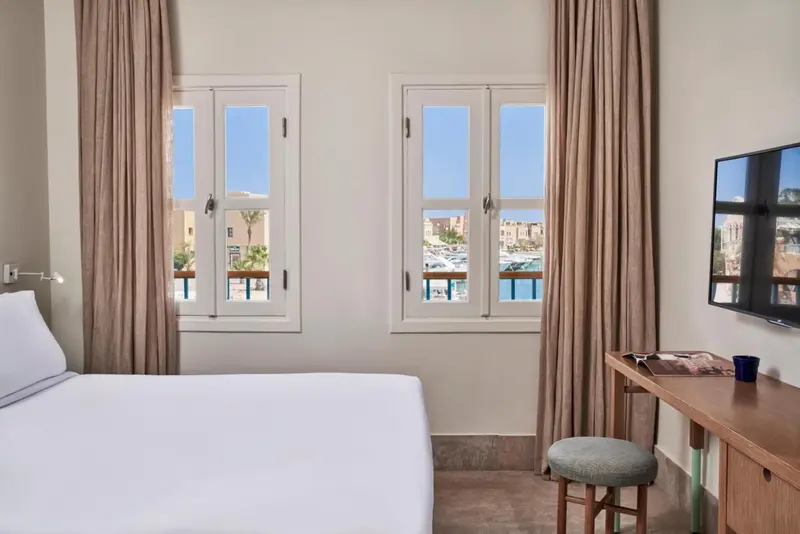 Une chambre lumineuse avec un lit blanc et un bureau près des fenêtres.