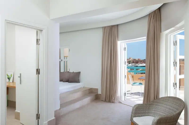 Une chambre lumineuse s'ouvre sur une terrasse avec vue sur un port de plaisance.