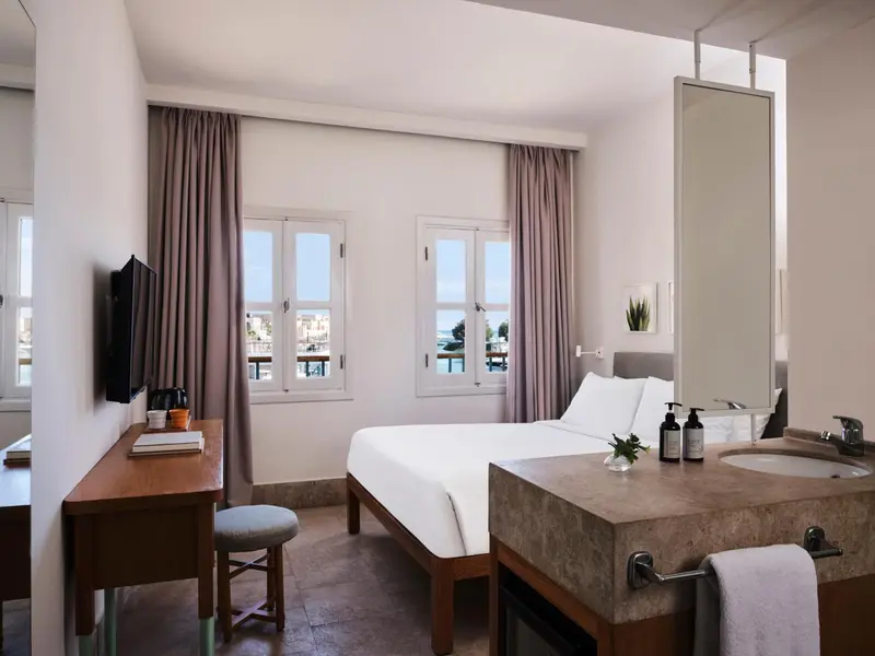 Une chambre lumineuse avec un lit et un bureau près des fenêtres.