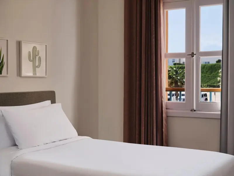 Une chambre lumineuse avec un lit simple et une fenêtre ouverte sur un paysage verdoyant.