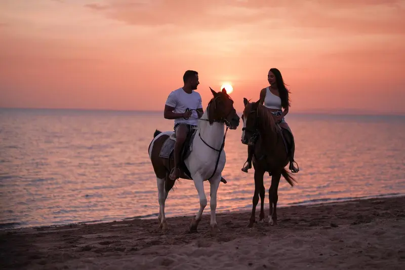 Deux personnes montent à cheval sur une plage au coucher du soleil.