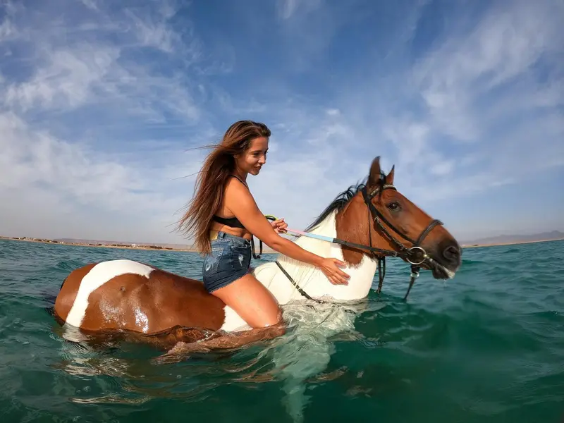 Une jeune femme à cheval dans l'eau turquoise.