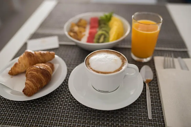 Un petit-déjeuner avec un croissant, des fruits et un café est présenté sur une table.