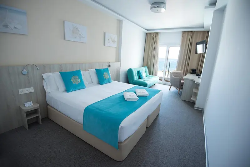 Chambre lumineuse avec un grand lit et un coin salon turquoise.