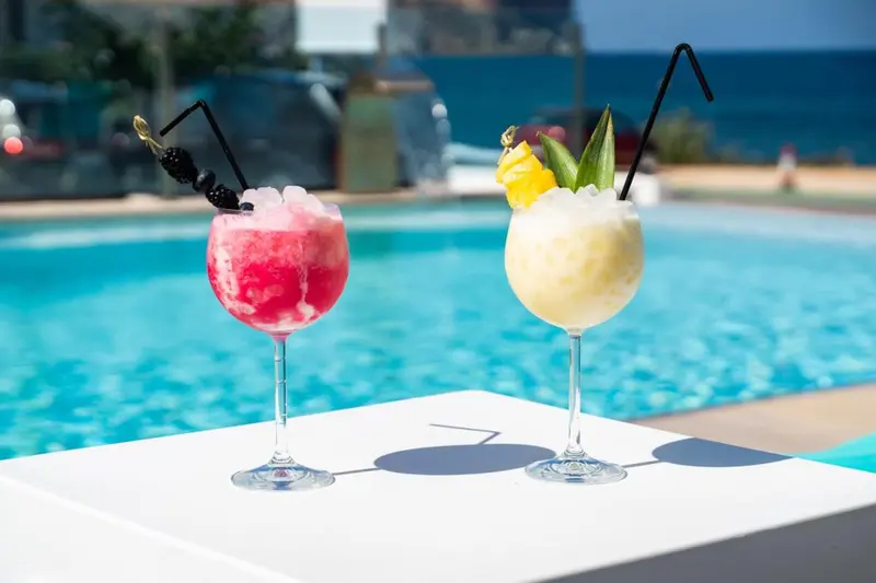 Deux cocktails colorés sont présentés au bord d'une piscine turquoise.