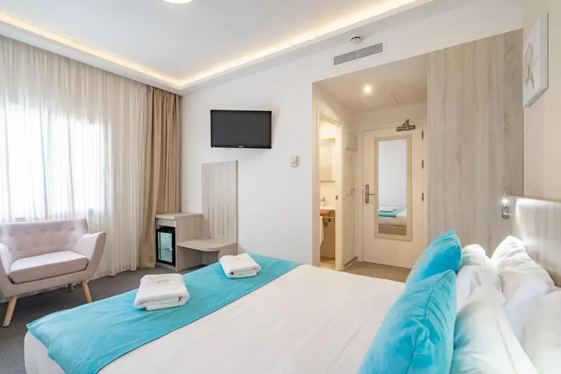 Une chambre lumineuse avec un lit fait et un coin salon.