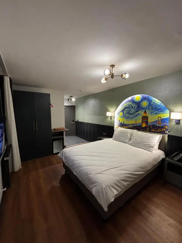 Une chambre avec un grand lit blanc et une décoration murale représentant un paysage nocturne.