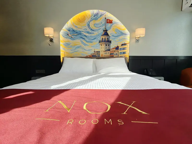 Lit double blanc dans une chambre d'hôtel décorée d'une fresque représentant un paysage urbain.