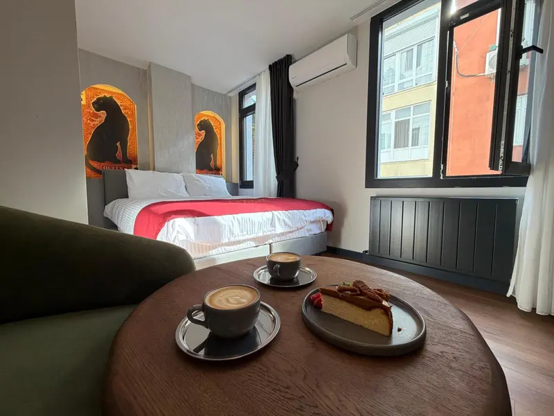 Une table basse avec des tasses de café et une part de gâteau se trouve devant un lit recouvert d'une courtepointe rouge.