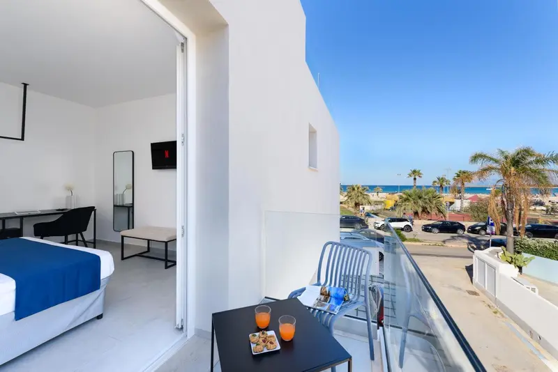 Une chambre lumineuse s'ouvre sur un balcon avec vue sur la mer et la plage.