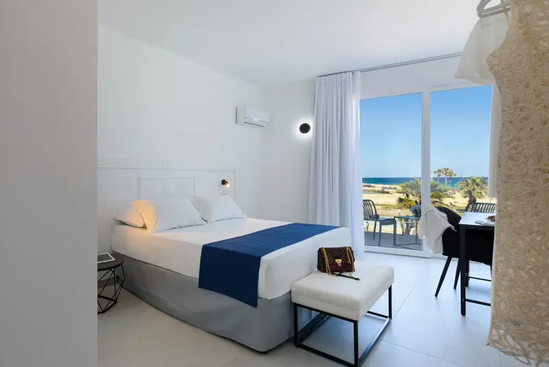 Chambre lumineuse avec un lit fait et une vue sur la mer par une baie vitrée.
