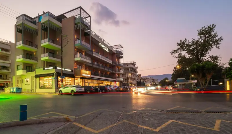 Bâtiment moderne avec des balcons illuminés au crépuscule, bordant une rue animée.