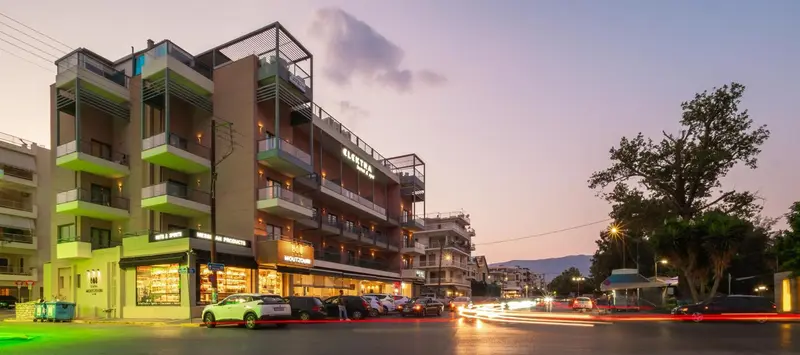 Bâtiment moderne avec des balcons et des commerces au rez-de-chaussée, éclairé au crépuscule.