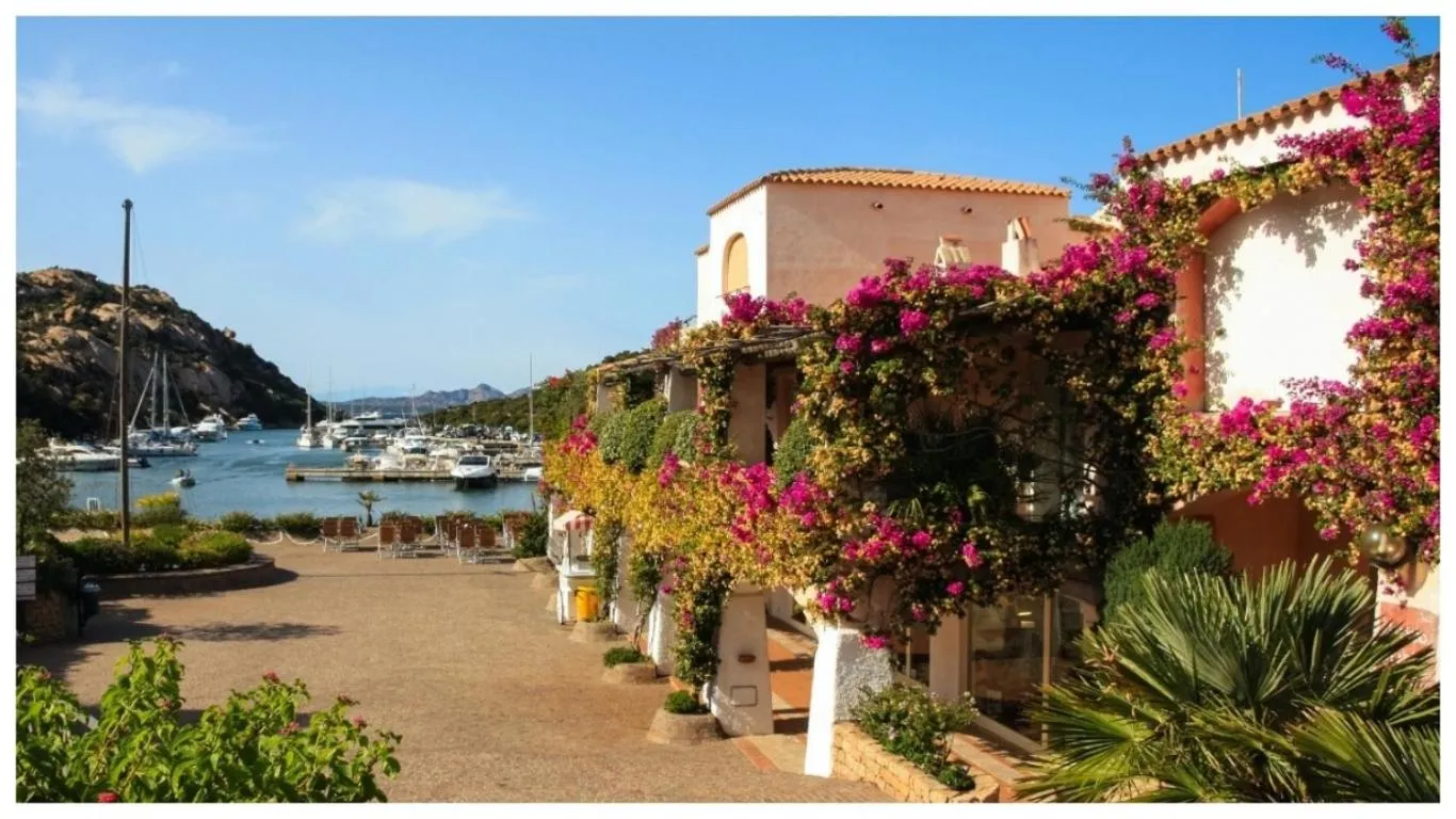 Bâtiment fleuri surplombant un port de plaisance ensoleillé.