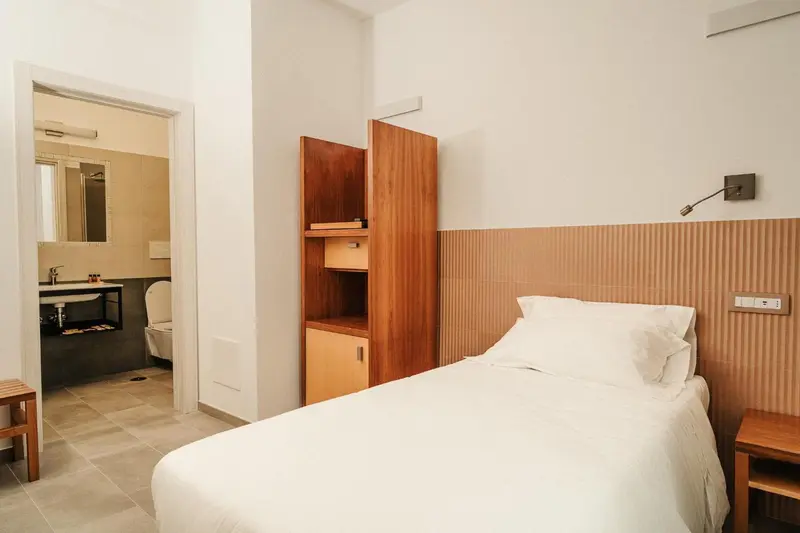Une chambre lumineuse avec un lit simple et un accès à une salle de bain.