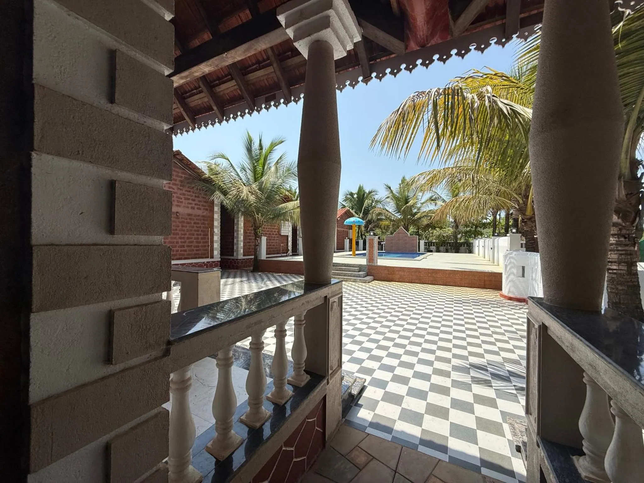 Terrasse ombragée donnant sur une cour carrelée et une piscine.