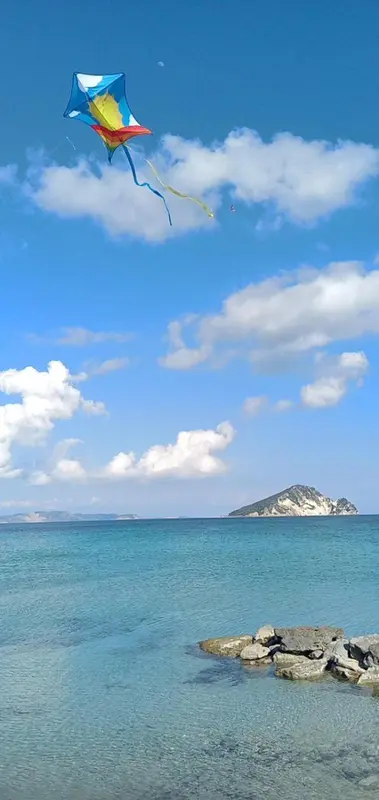 Ciel bleu avec un cerf-volant coloré au-dessus d'une plage rocheuse.