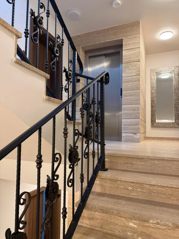 Escalier en pierre avec rampe en fer forgé et ascenseur en fond.