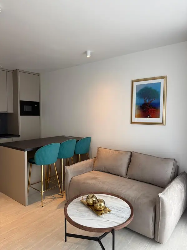 Un salon moderne avec un canapé gris et un bar avec des tabourets verts.
