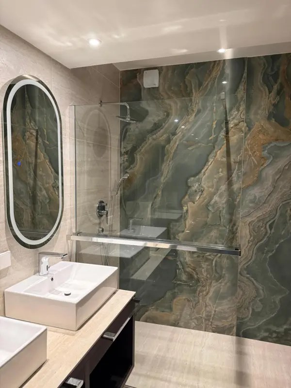 Une salle de bain moderne avec une douche à l'italienne et un grand miroir ovale.