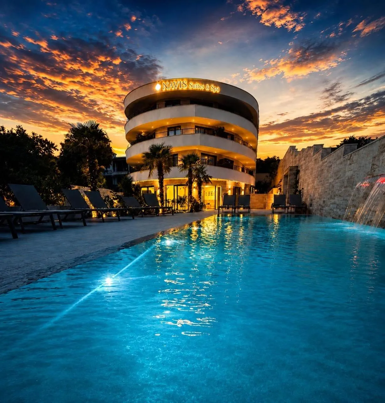 Bâtiment moderne avec piscine illuminée au premier plan, au coucher du soleil.