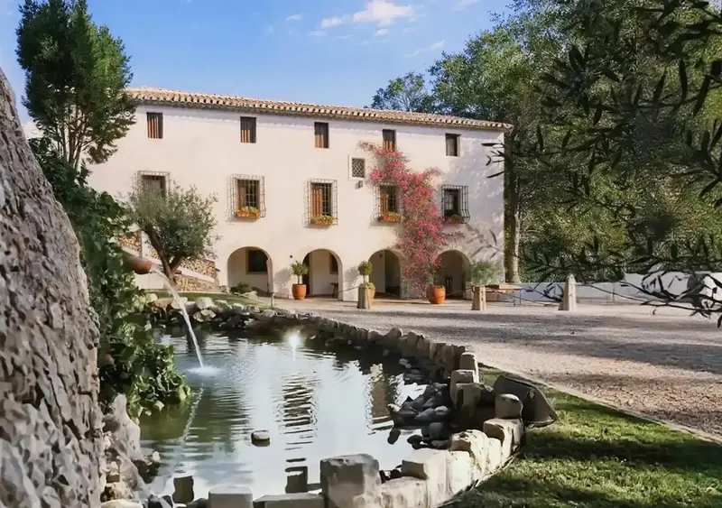 Bâtiment en pierre claire avec des ouvertures en arc, entouré de végétation et d'une fontaine.