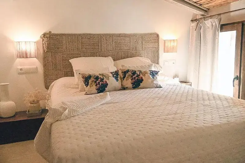Un lit double avec une tête de lit en osier et des oreillers décorés.