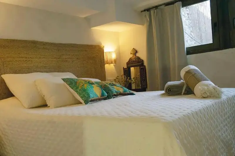 Une chambre lumineuse avec un grand lit recouvert d'une courtepointe blanche et de coussins colorés.