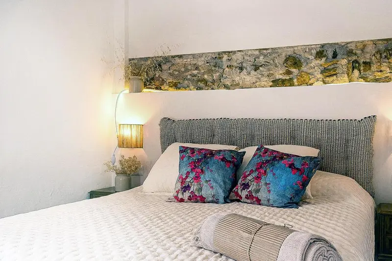 Une chambre lumineuse avec un grand lit recouvert d'une couette blanche et de coussins colorés.