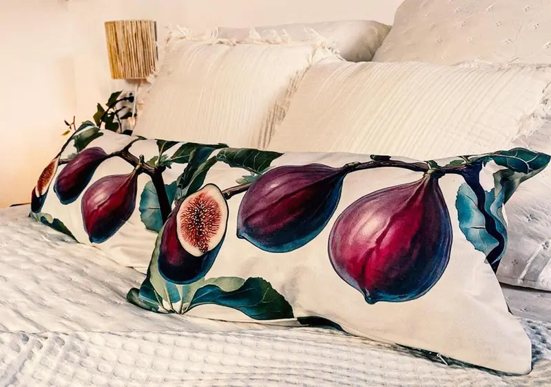 Un lit recouvert d'une couette blanche et orné d'un long coussin à motif de figues.