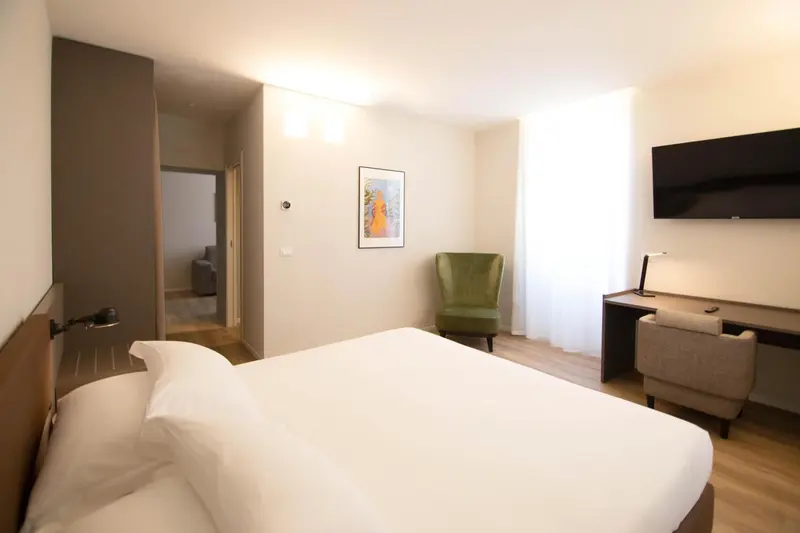 Une chambre lumineuse avec un lit blanc et un fauteuil vert.