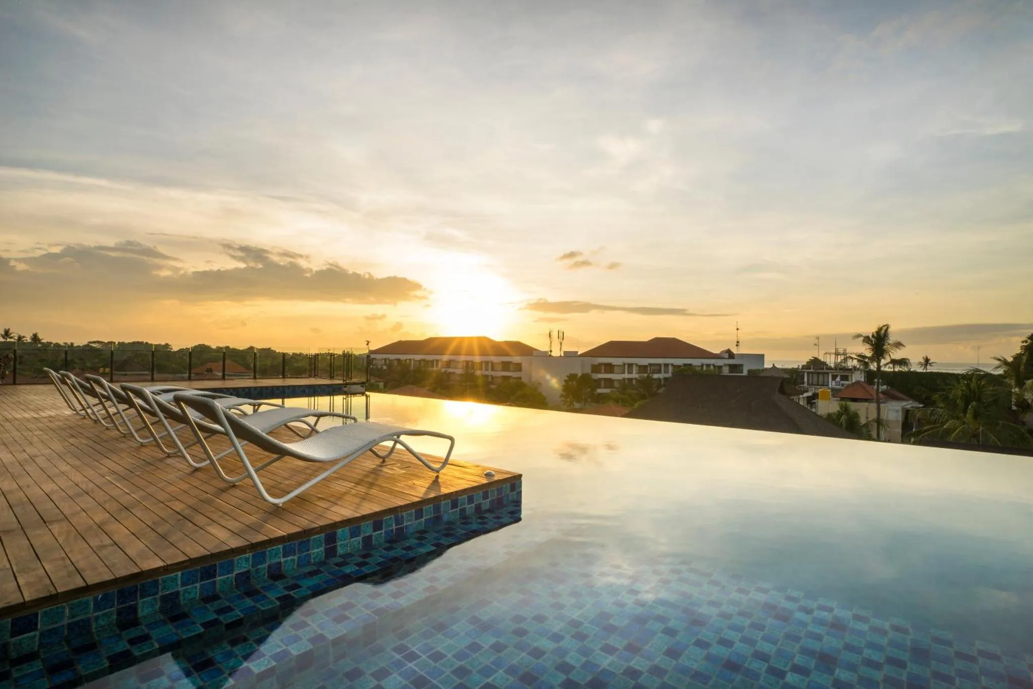 Transats alignés au bord d'une piscine à débordement avec vue sur le coucher de soleil.