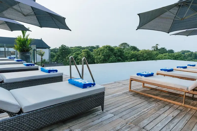 Transats blancs et parasols ombragent une piscine rectangulaire bordée d'une terrasse en bois.