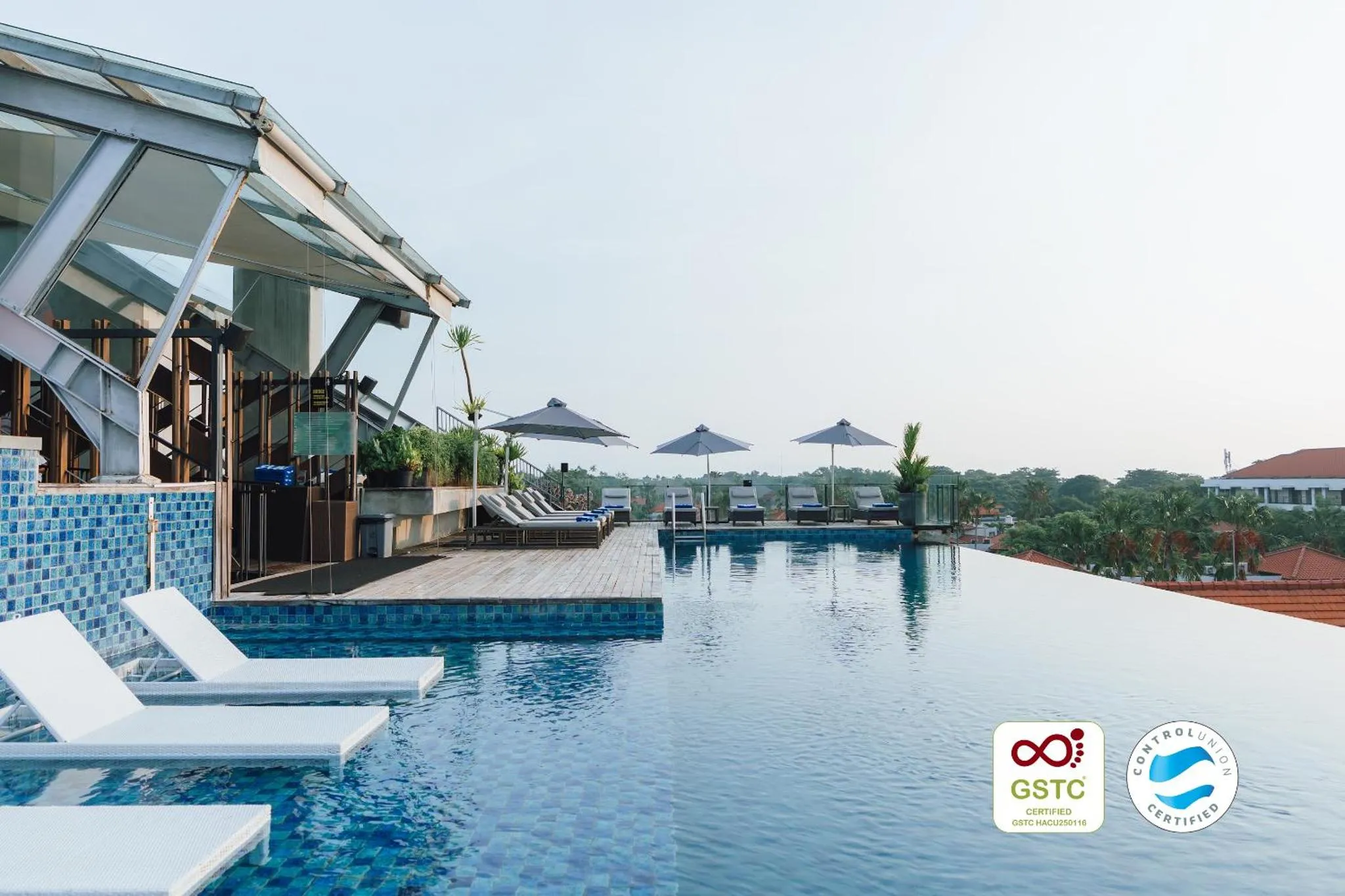 Piscine à débordement avec transats et parasols dans un cadre tropical.