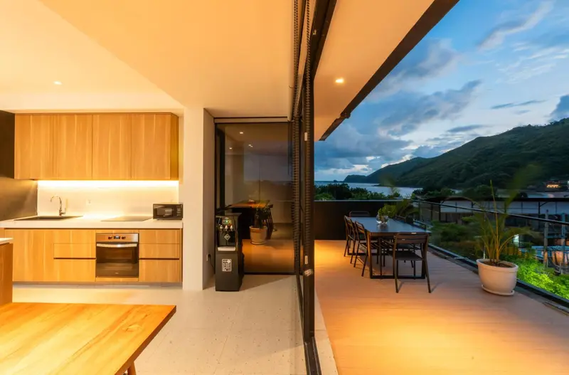 Une cuisine moderne s'ouvre sur une terrasse avec vue sur la mer et les montagnes.