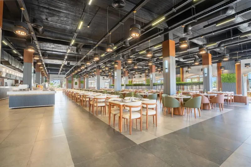 Une grande salle lumineuse avec de nombreuses tables et chaises disposées pour les repas.