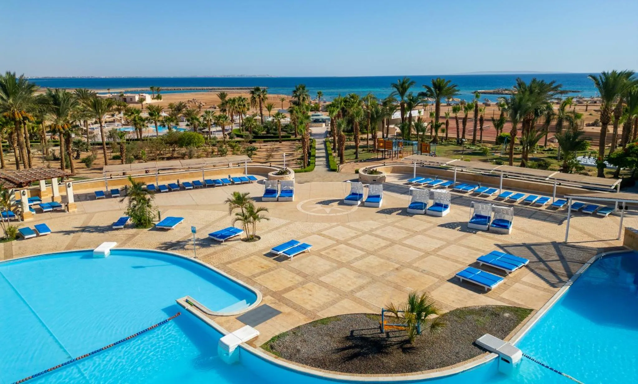 Vue aérienne d'un complexe hôtelier avec piscine et transats face à la mer.