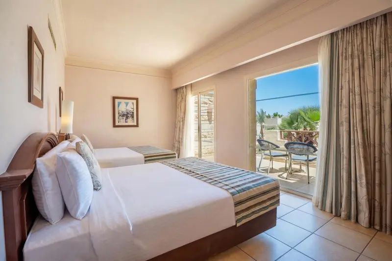 Chambre lumineuse avec deux lits et balcon donnant sur une végétation luxuriante.