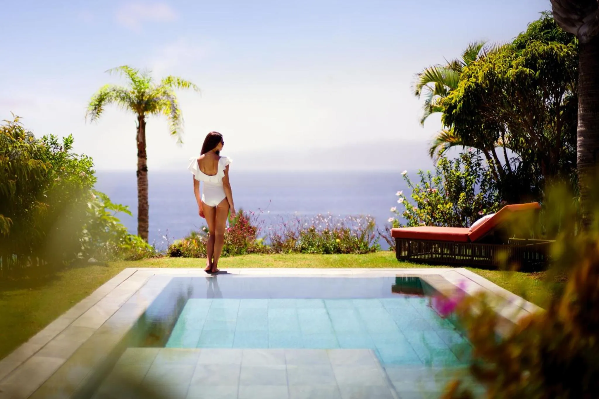 Une femme se tient au bord d'une piscine avec vue sur la mer.