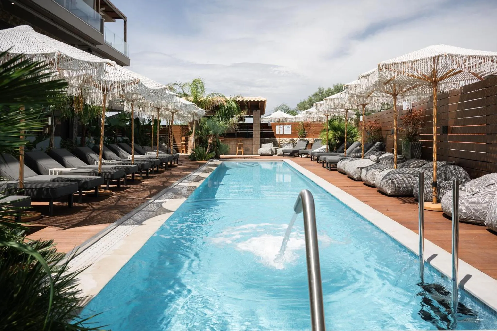 Transats et parasols ombragent une piscine rectangulaire bordée d'une terrasse en bois.